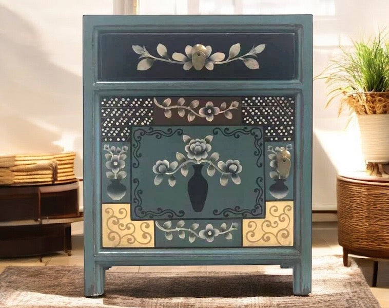 Frontalansicht eines bemalten Nachttisches in Petrol mit zentralem Blumenmuster in Vasenmotiv, goldverzierten Details und floralem Dekor.