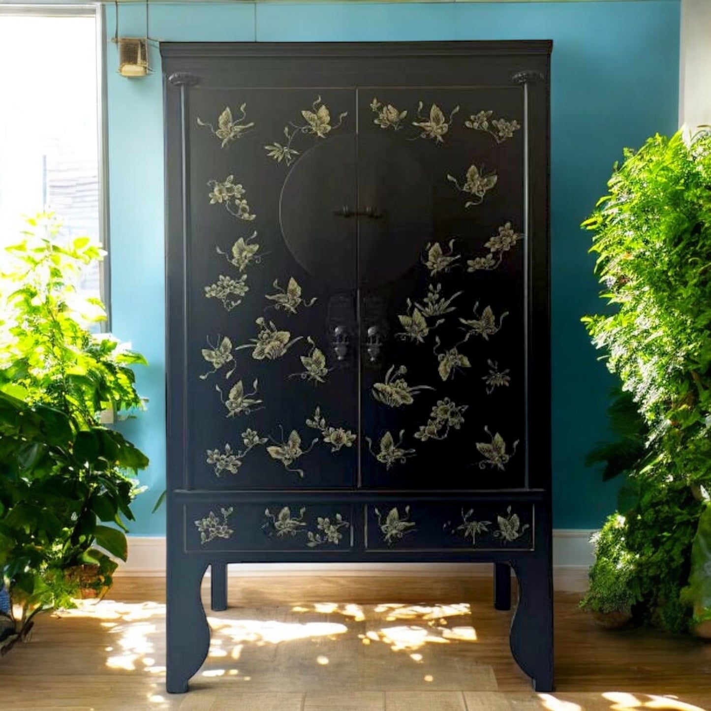 Schwarzer asiatischer Schrank mit goldenen Schmetterlings- und Blumenmotiven, dekorativ im Raum platziert.