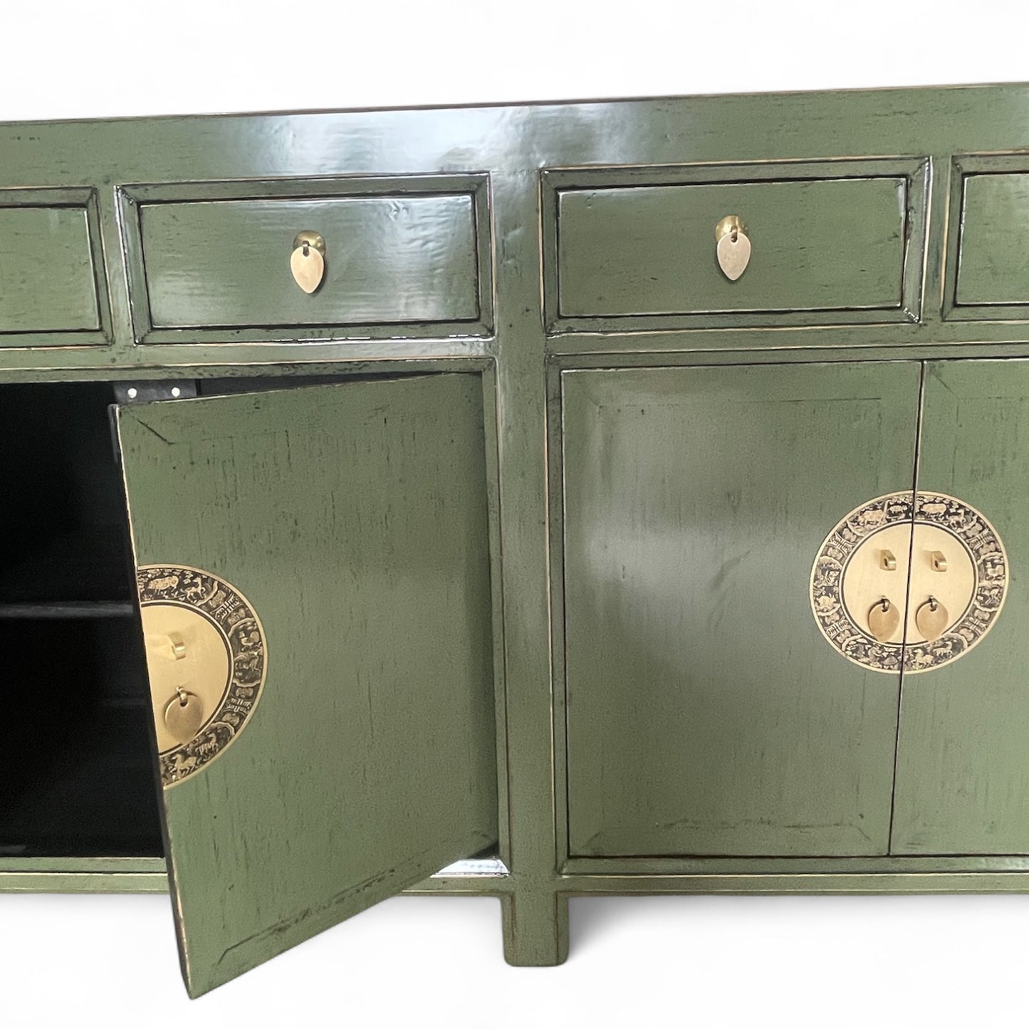 Teilansicht eines grünen Sideboards mit geöffnetem linken Schrankfach und runder Messingbeschlag-Verzierung.
