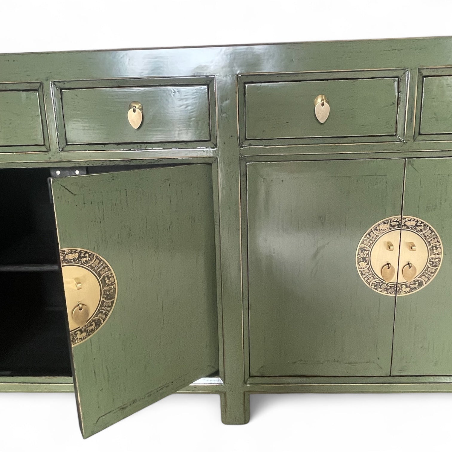Teilansicht eines grünen Sideboards mit geöffnetem linken Schrankfach und runder Messingbeschlag-Verzierung.