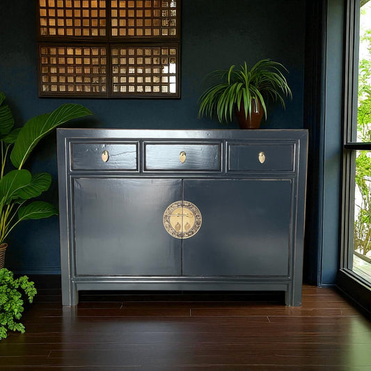Dunkelblaue Kommode im asiatischen Stil, vor dunkler Wand mit Topfpflanzen und stilvoller Dekoration.